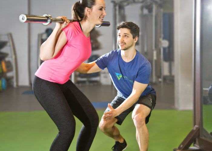 Personal Fitness Trainer Tom Franke unterstützt Kundin bei der Kniebeuge im Krafttraining