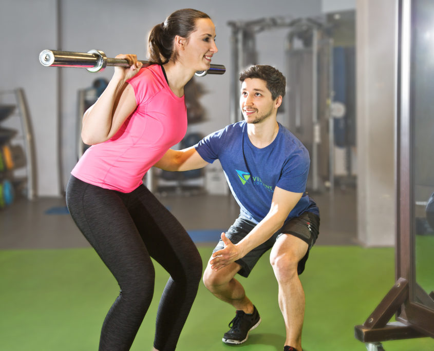 Personal Fitness Trainer Tom Franke unterstützt Kundin bei der Kniebeuge im Krafttraining